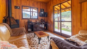 Ein gemütliches Blockhaus-Interieur mit Holzwänden, Kamin, Sofa, Couchtisch und Blick ins Freie.