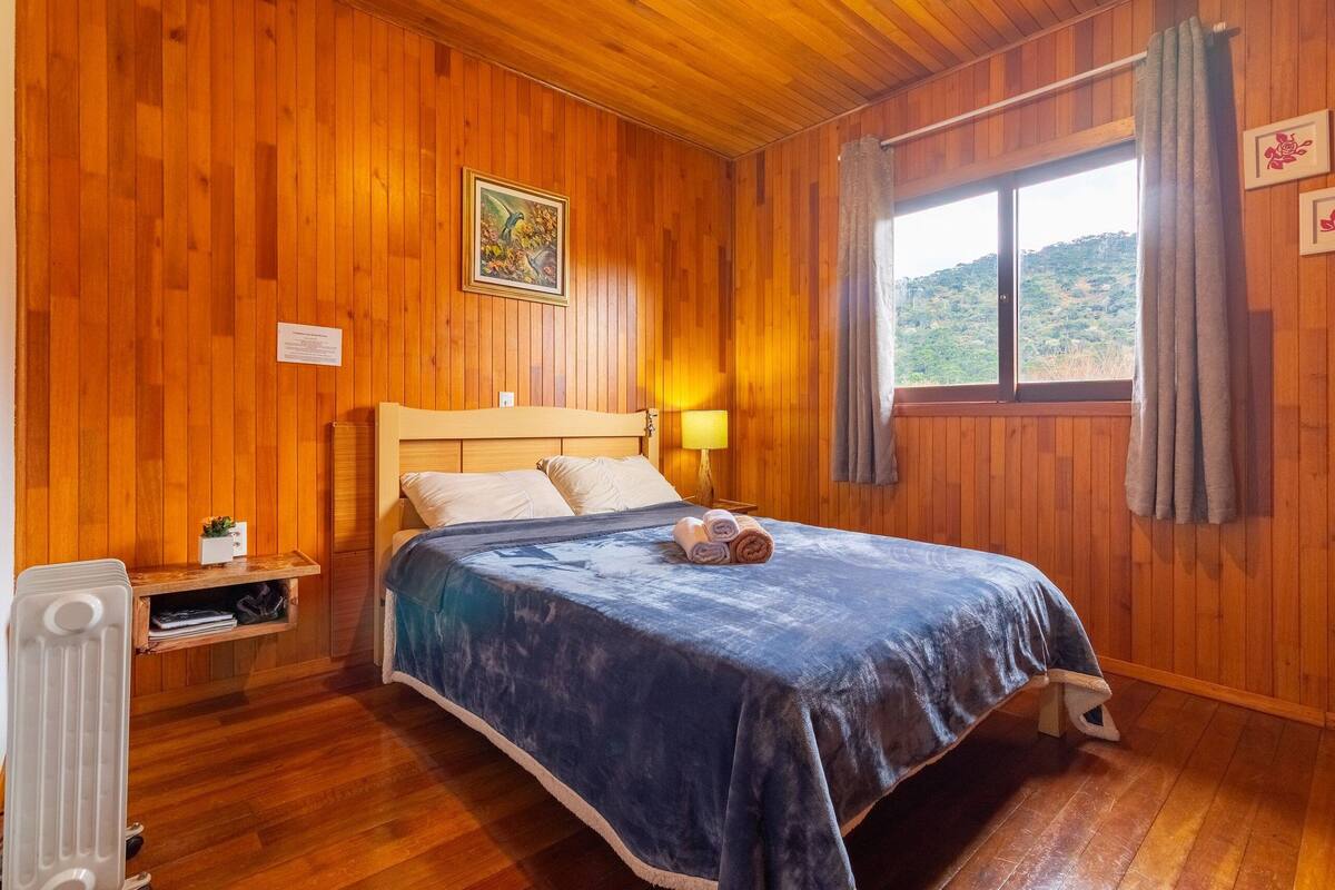 Habitació amb panells de fusta, un llit, una taula de nit, una finestra amb cortines i vista a l'exterior.