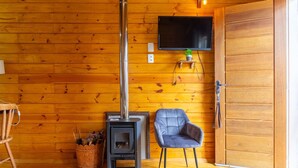 Ein Zimmer mit Holzwänden, einem schwarzen Kaminofen, einem angebrachten Fernseher und einer Tür.