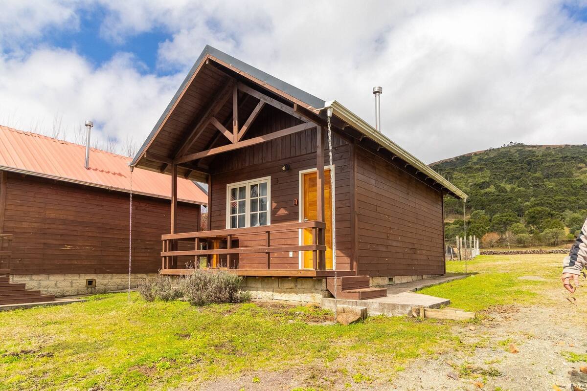 Una cabana de fusta amb un porxo, una xemeneia i un paisatge de pendent al fons.