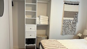 Une chambre à coucher avec un lit, une armoire blanche, un ventilateur de plafond, une tapisserie tissée et une petite table ronde.