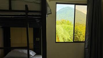 A room with a bunk bed, a window with a view of greenery and hills, and a tiled floor.