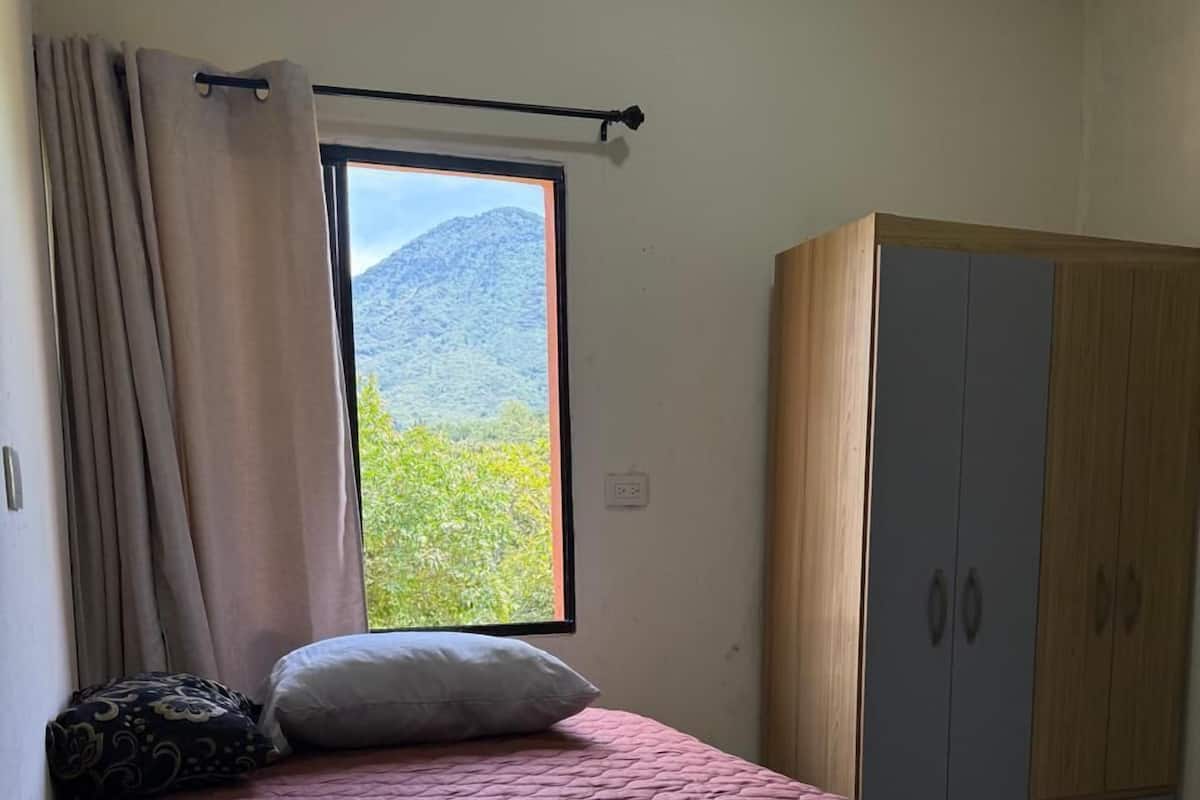 A bedroom with a bed, a wardrobe, and a window with a mountain view.