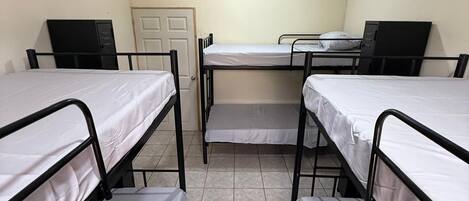 A dormitory room with four bunk beds, a desk, and a chair.