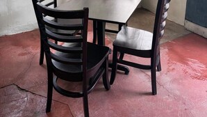A room with a table and four chairs, large windows with metal bars, and a view of greenery outside. - Villa San Carlos (Juayua)