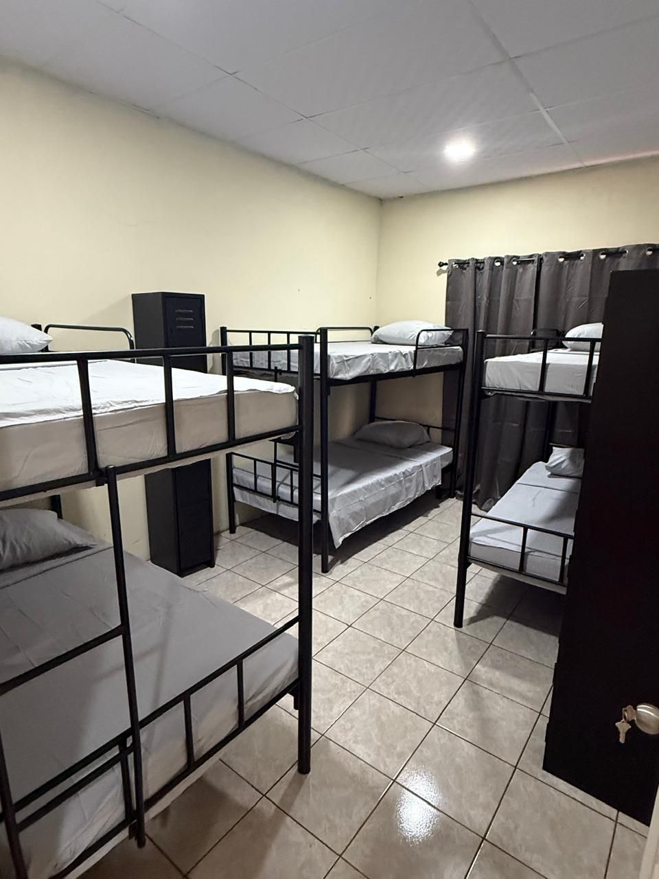 A dormitory room with bunk beds, a cabinet, and a curtain.