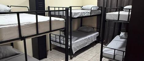 A dormitory room with bunk beds, a cabinet, and a curtain.