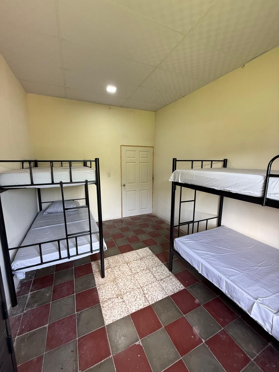 Un dormitorio con dos literas, piso de baldosas y una puerta.