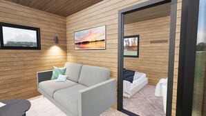 A modern room with wooden panel walls, a grey sofa with patterned cushions, a bed with white bedding, and a framed picture of a sunset. - Luxury lodges with views of Lancashire rolling hills & our beautiful golf course (Staining)