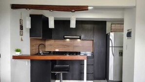 A modern kitchen with dark cabinetry, a wooden countertop, a stainless steel refrigerator, and pendant lighting. - Comfortable apartment south cali - valle de lilí with nature view (Cali)