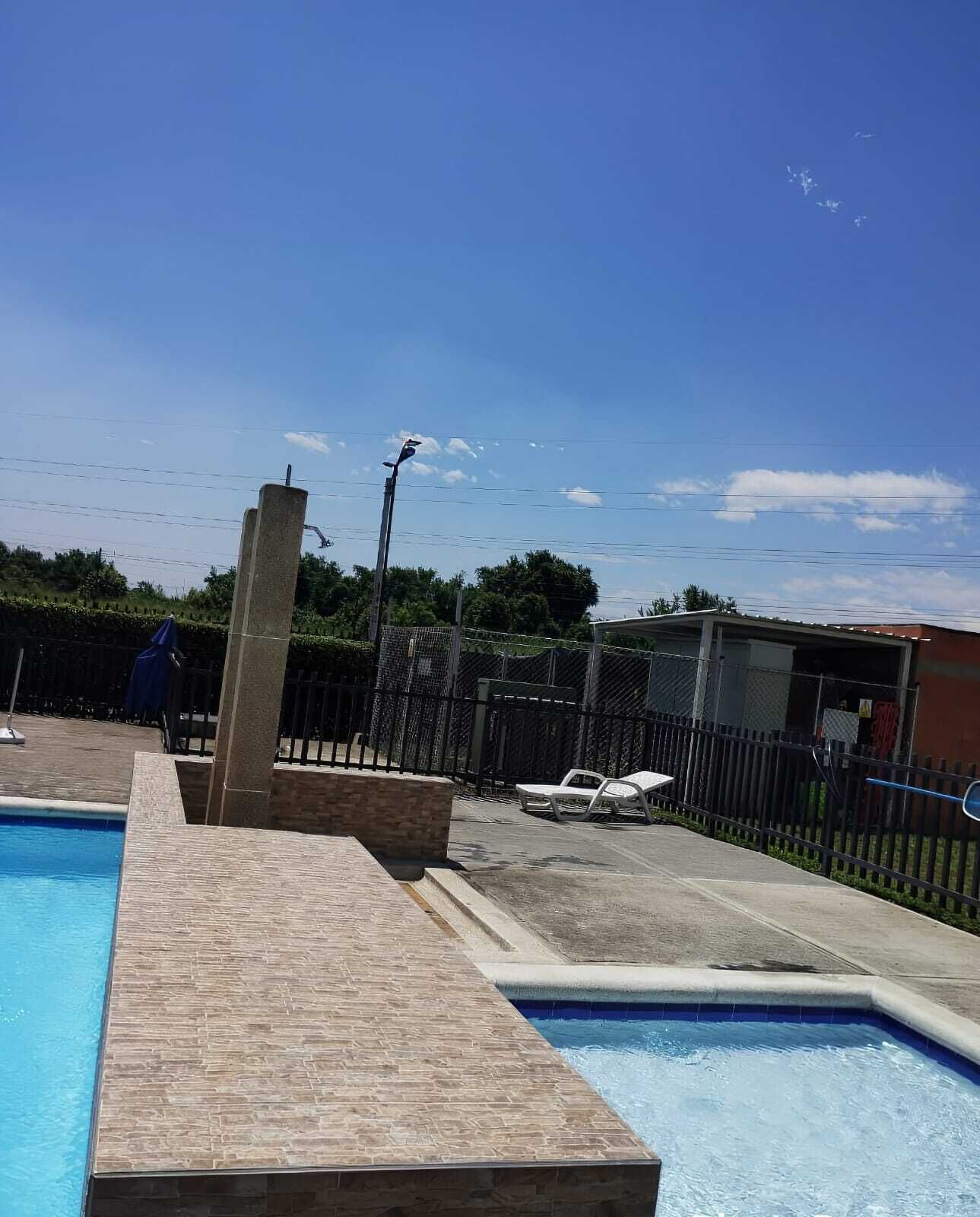 A swimming pool with a tiled deck, a concrete structure, and a fenced area with lounge chairs.