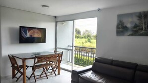 A modern living room with a dining area, a sofa, a TV, and a balcony with a view of greenery. - Comfortable apartment south cali - valle de lilí with nature view (Cali)