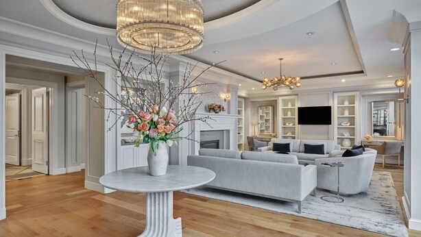 Un salon moderne avec un canapé gris, une table ronde ornée d’un vase de fleurs et un lustre.