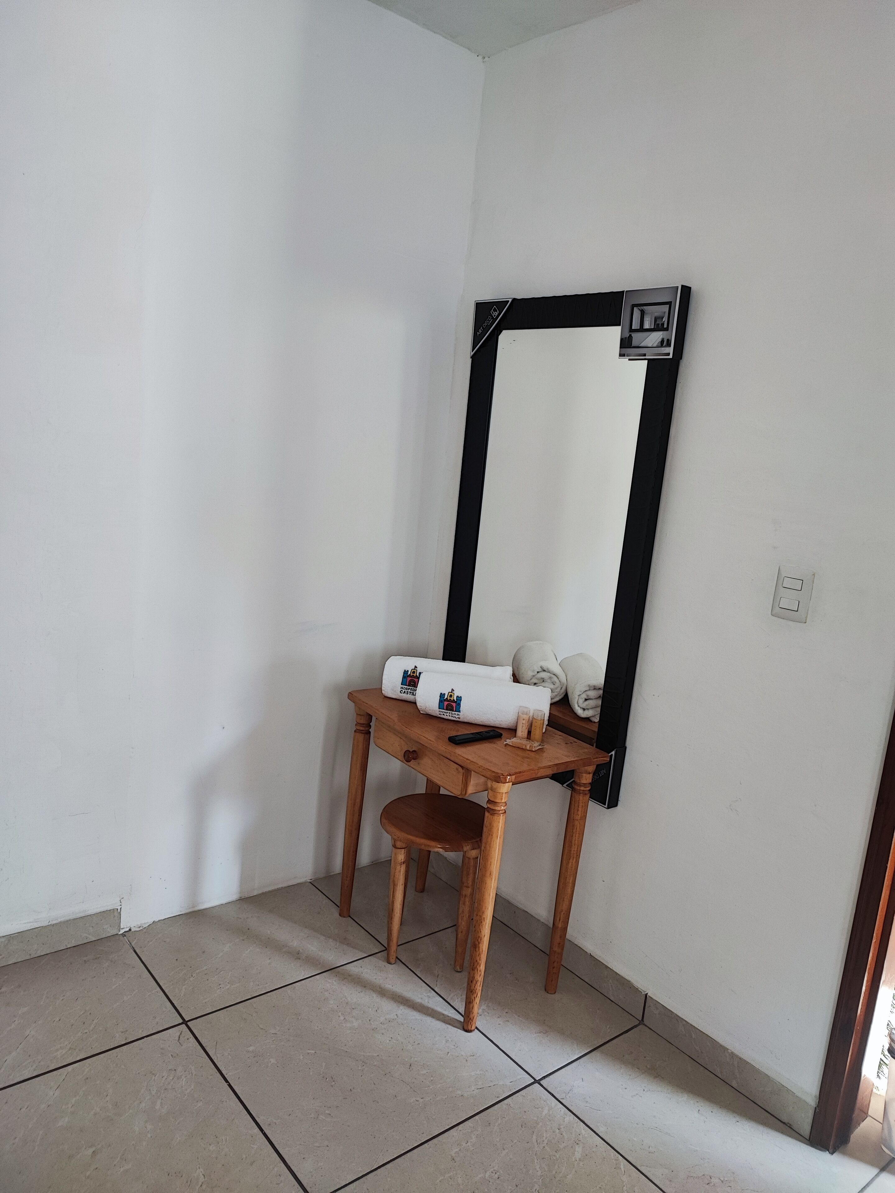 Ein Eckzimmer mit einer Holzbank, einem Spiegel mit schwarzem Rahmen und einem kleinen Tisch mit Handtüchern und einer Fernbedienung.