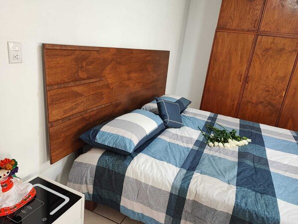 A bedroom with a wooden headboard, a checkered bedspread, and a bedside table with a decorative item.