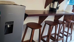 Ett kök med träskåp, ett kylskåp i rostfritt stål, en kaffebryggare och en vattenautomat.