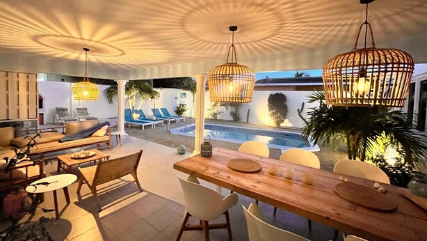 A modern outdoor dining area with a pool, lounge chairs, and hanging lights. - *NEW* Cozy Casa! Tasteful family villa with private pool! (Oranjestad)
