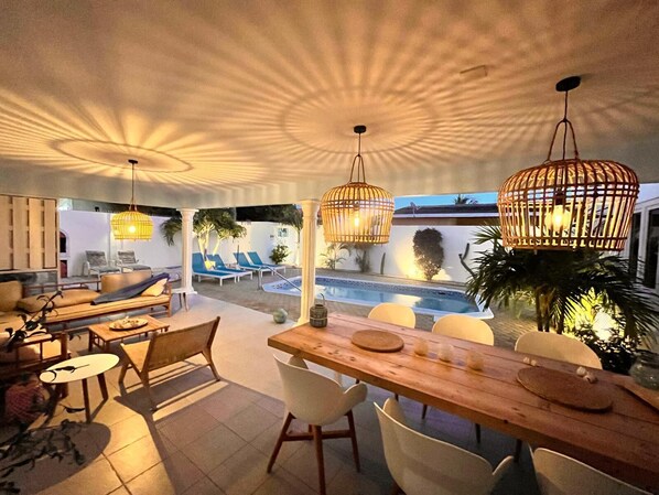 A modern outdoor dining area with a pool, lounge chairs, and hanging lights.