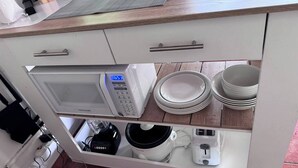 Eine Küche mit Mikrowelle, Kaffeemaschine und gestapelten Tellern.