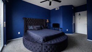Ein Schlafzimmer mit einem gepolsterten Kopfteil, einem runden Bett, einem Deckenventilator und einem Fernseher auf einem Sockel.