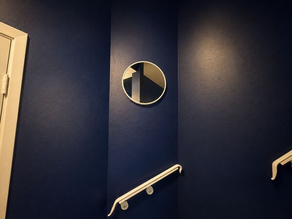 A bathroom with a dark blue wall, a round mirror, and a white handrail.