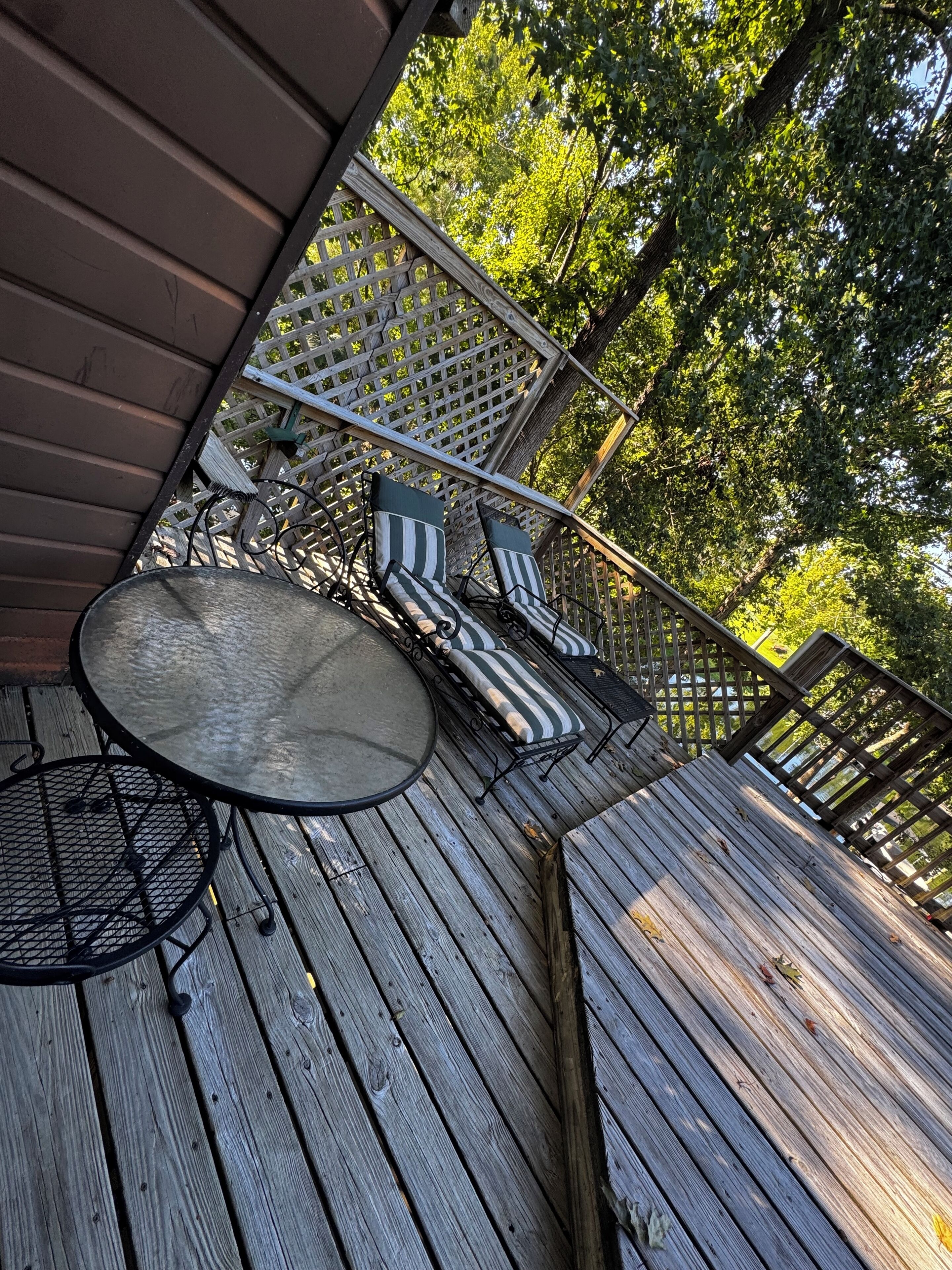 A wooden deck with a round table and two striped lounge chairs.
