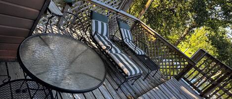 A wooden deck with a round table and two striped lounge chairs.