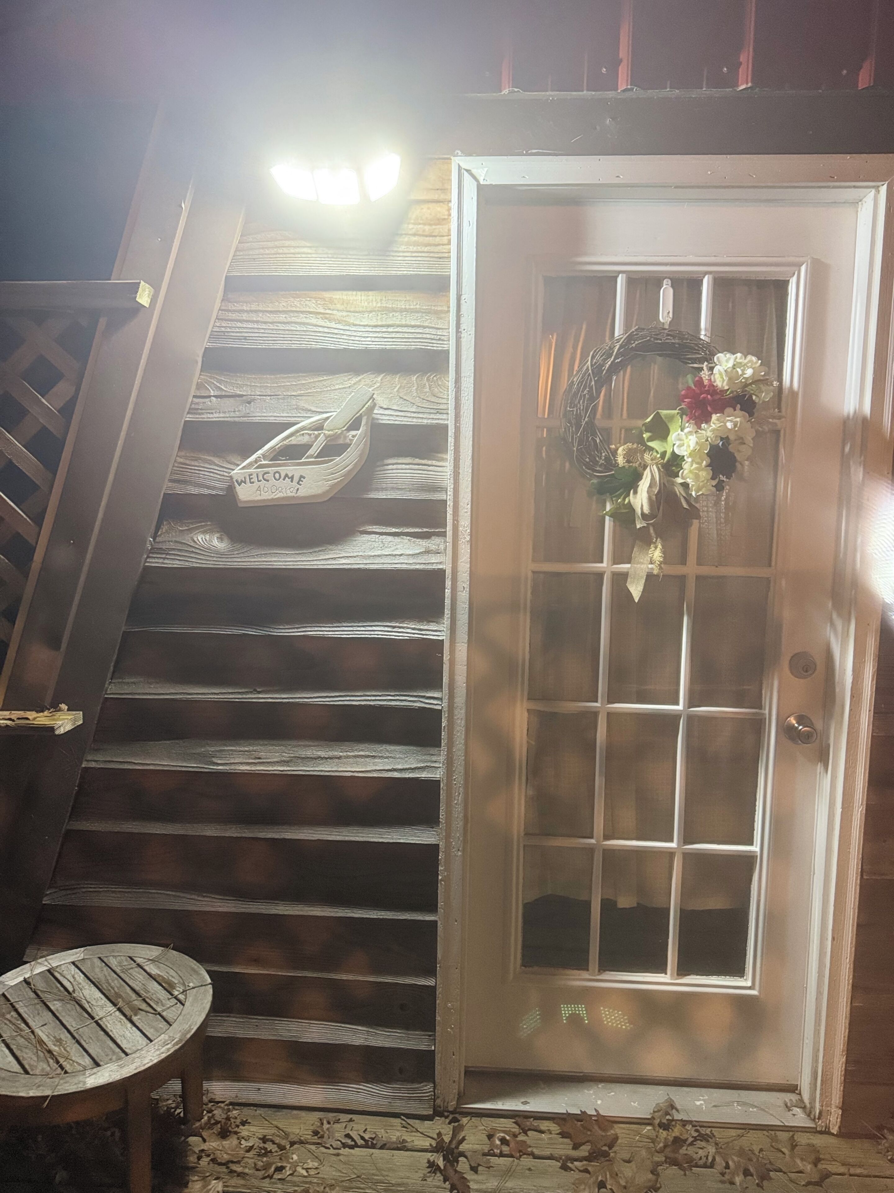 Un escalier en bois mène à une porte dotée d’un panneau de verre et ornée d’une guirlande. Une petite table est placée sur le côté gauche de l’escalier.