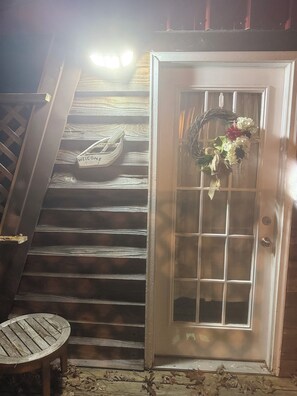 Un escalier en bois mène à une porte dotée d’un panneau de verre et ornée d’une guirlande. Une petite table est placée sur le côté gauche de l’escalier.
