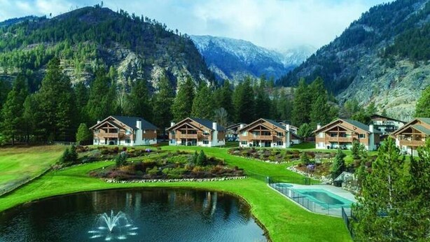 A resort with multiple wooden cabins, a central pond with a fountain, and a mountainous backdrop. - Enjoy Oktoberfest in this Charming 2-bedroom condo in fabulous Leavenworth (Leavenworth)