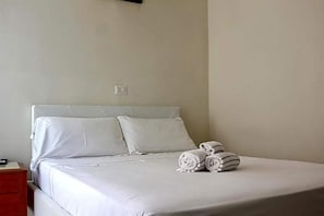 Un lit bien fait, avec du linge de lit blanc et des oreillers, une table de chevet avec une lampe et des serviettes pliées posées sur le lit.