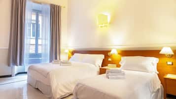Una habitación de hotel con dos camas, una ventana con cortinas y lámparas fijadas a la pared.