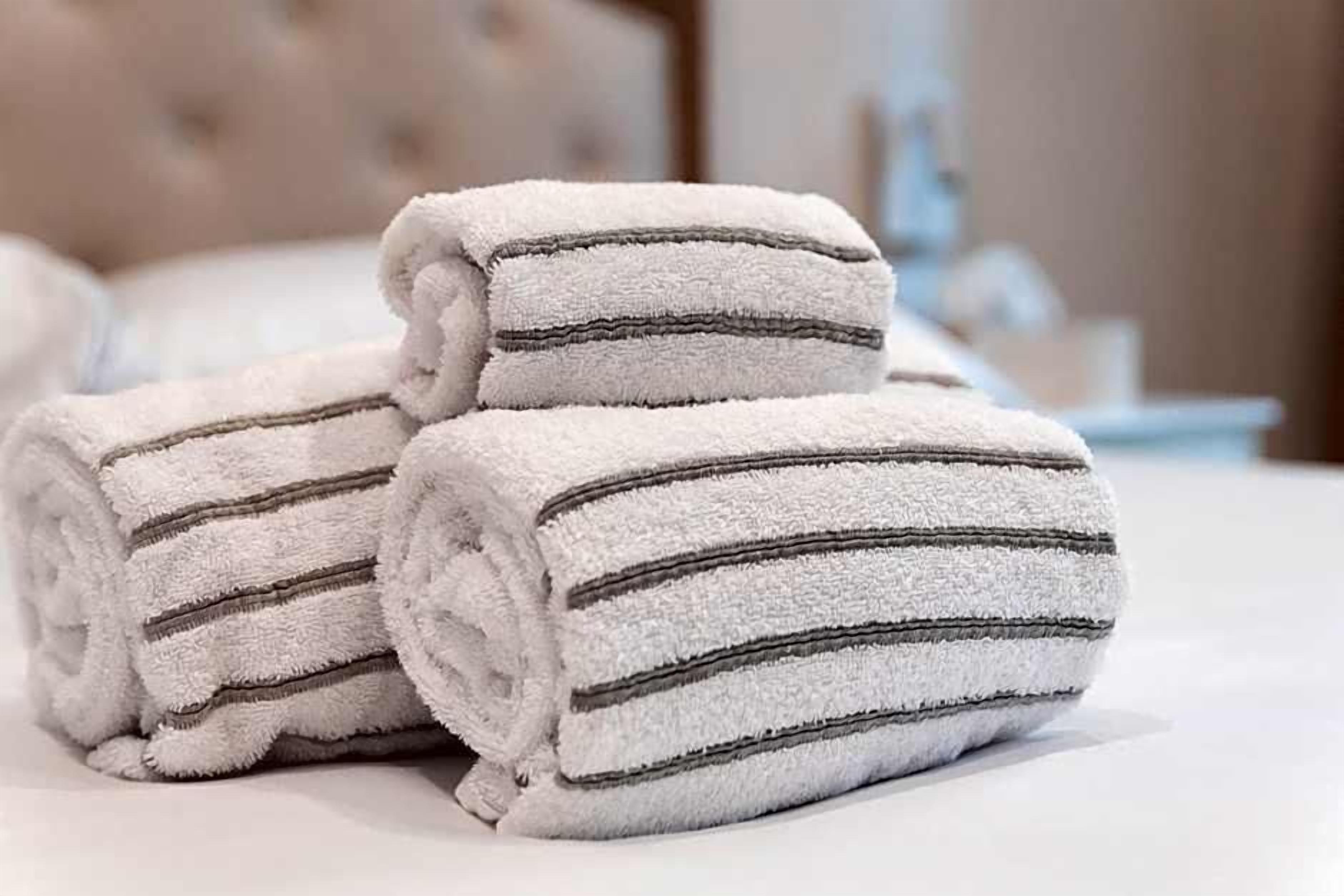 Three rolled towels with dark stripes on a bed.