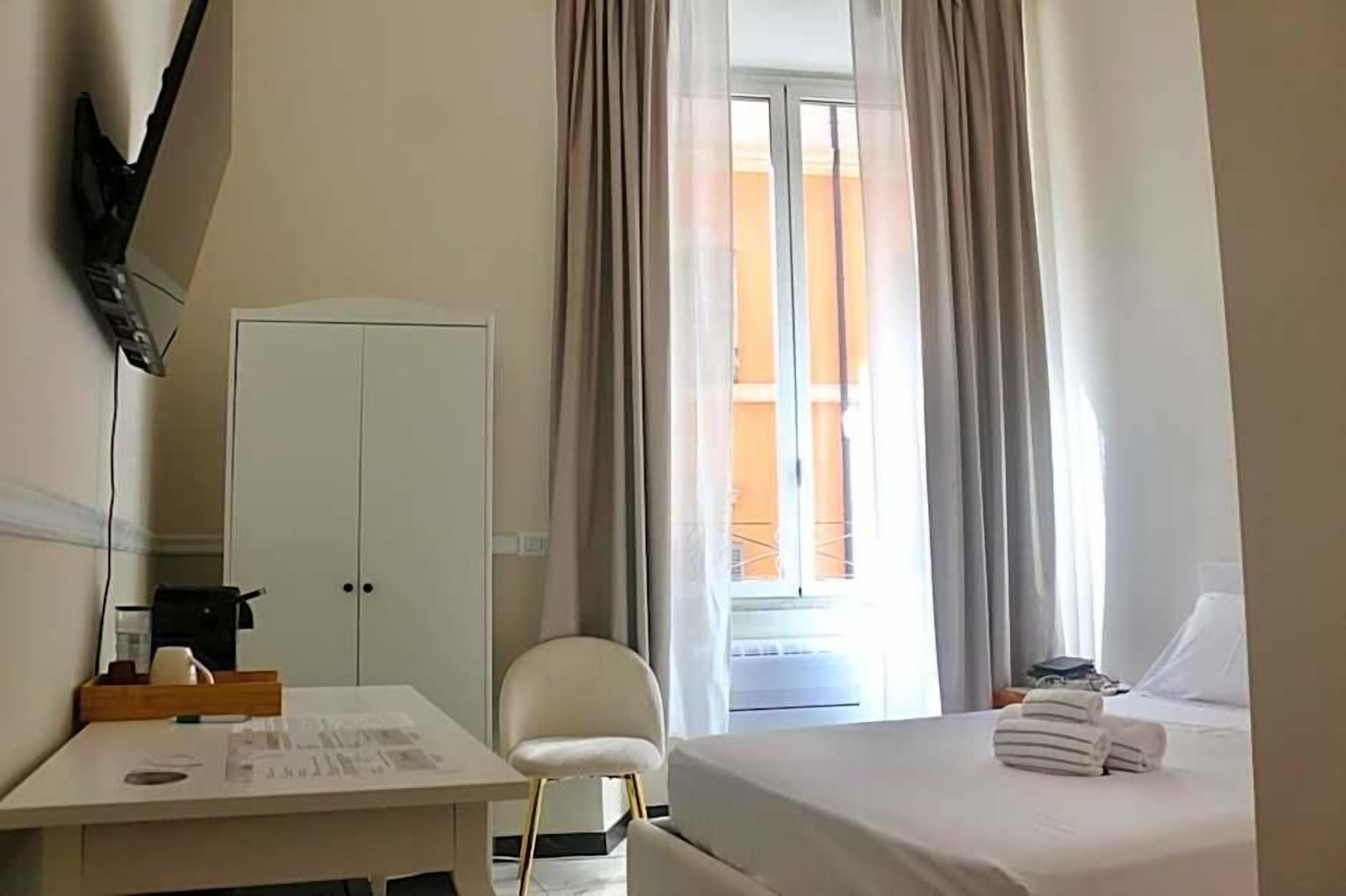 A hotel room with a bed, a desk, a chair, a wardrobe, and a window with curtains.