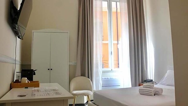 A hotel room with a bed, a desk, a chair, a wardrobe, and a window with curtains. - Hotel Domus Rome (Rome)