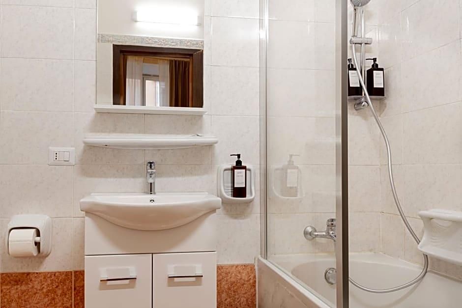 A bathroom with a sink, mirror, shower, and toiletries.