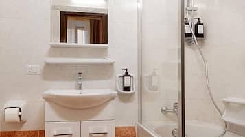 A bathroom with a sink, mirror, shower, and toiletries.