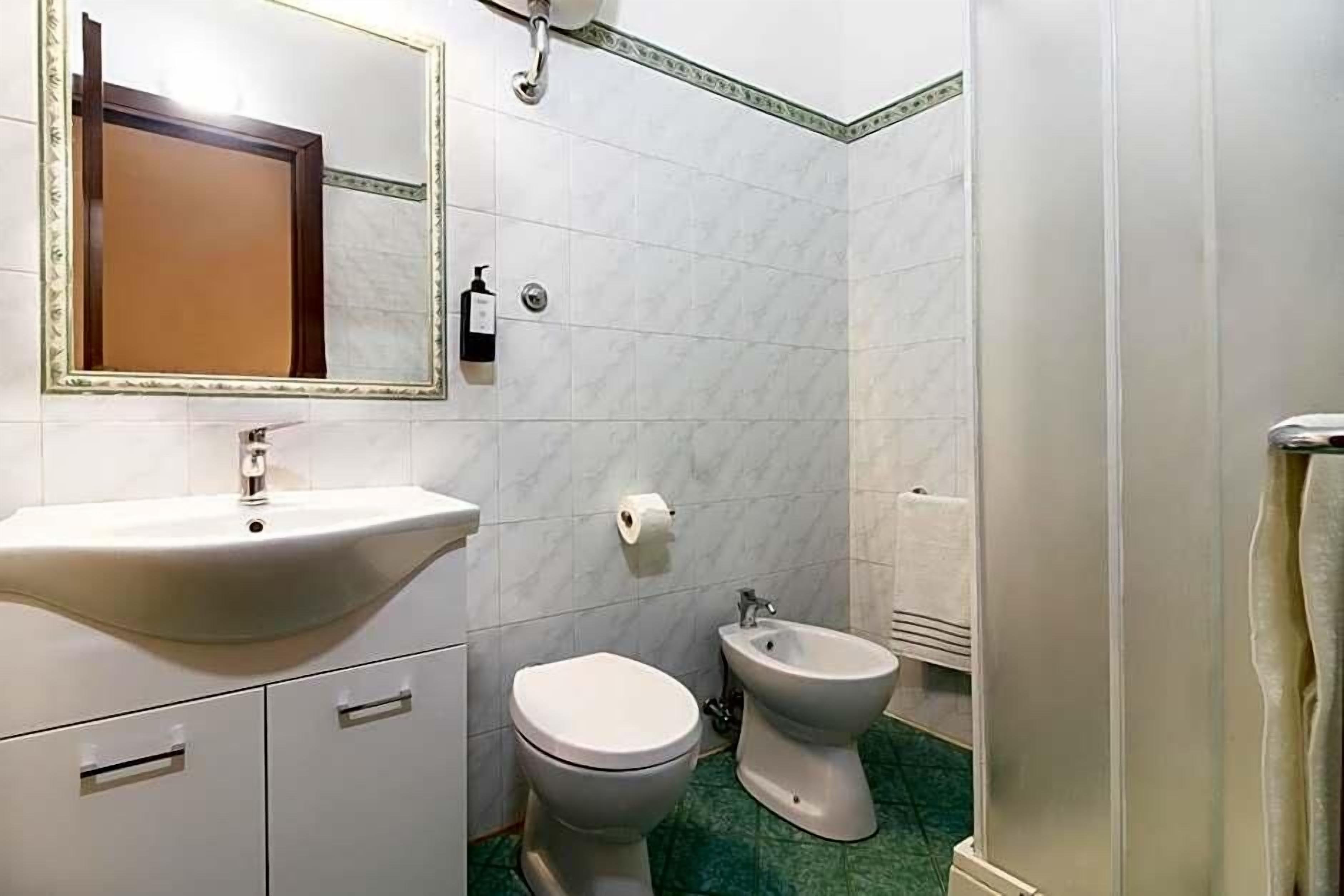 Un baño con lavamanos, inodoro, bidé y un espejo con marco decorativo.