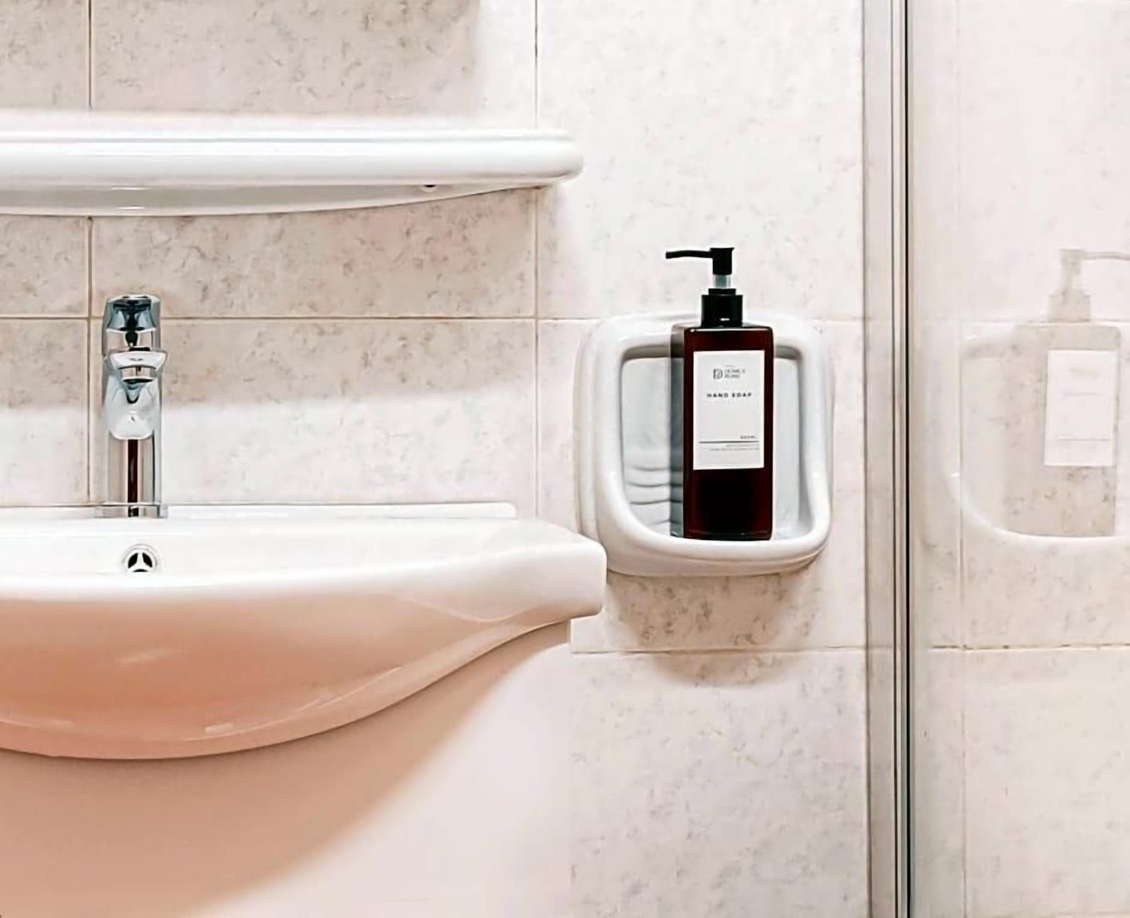 A bathroom with a white sink, a hand soap dispenser, and a soap dispenser on the wall.