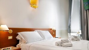 A hotel room with a neatly made bed, two bedside lamps, a small bedside table with a book, and a window with curtains. - Hotel Domus Rome (Rome)