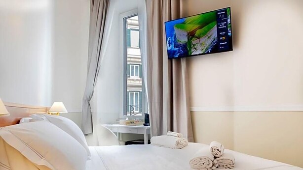 A hotel room with a bed, a desk, a TV, and a window with curtains. - Hotel Domus Rome (Rome)