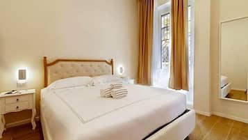 Una cama bien tendida con cabecera de madera, una mesita de noche con lámpara y una ventana con cortinas.