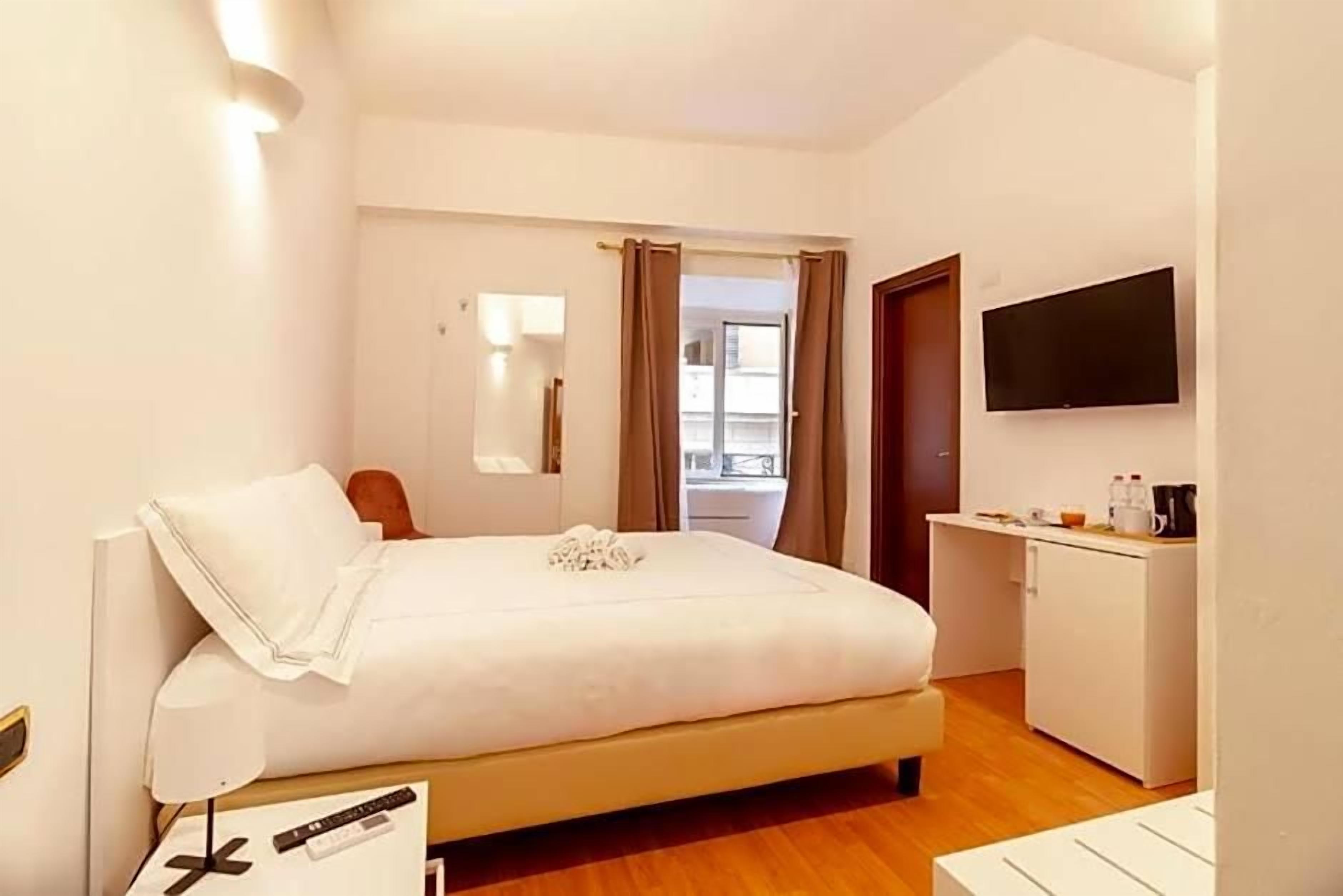 A hotel room with a bed, bedside table, lamp, TV, and a small kitchenette.