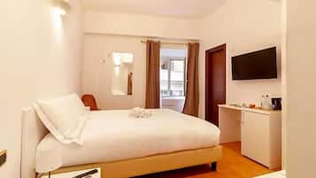 A hotel room with a bed, bedside table, lamp, TV, and a small kitchenette.