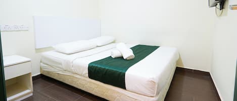 A neatly made bed with a green blanket and white linens, a bedside table, and a wall-mounted TV.