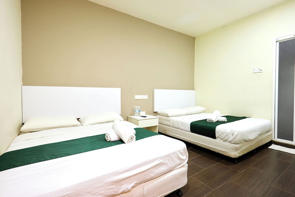 Una habitació d'hotel amb dos llits, un corredor verd al llit, roba de llit blanca, una nit del taulell amb un telèfon i una ampolla, i una porta corredissa de vidre.