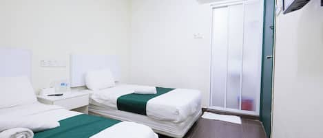 A hotel room with two beds, a wardrobe, an air conditioning unit, and a small table with a remote control.