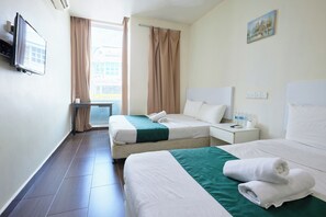 Ein Hotelzimmer mit zwei Betten, einem Fernseher, einem Fenster mit Vorhängen, einem Bild an der Wand und einem Nachttisch mit Fernbedienung und Wasserflaschen.