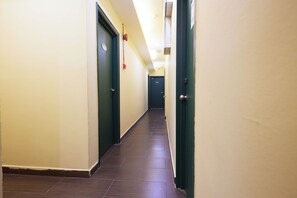 Un couloir avec des portes de part et d’autre, un sol carrelé et un luminaire au plafond.