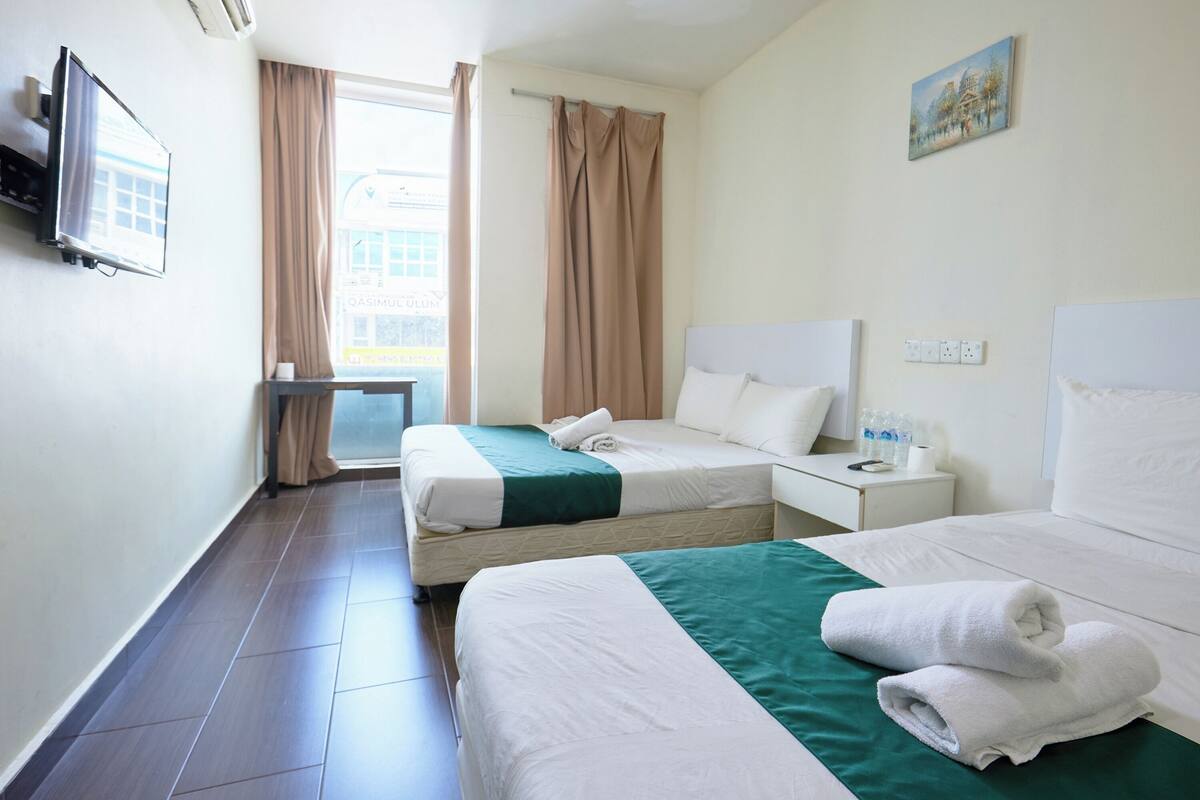 Habitació d'hotel amb dos llits, una televisió, una finestra amb cortines, un quadre a la paret i una taula de nit amb un telèfon i ampolles d'aigua.